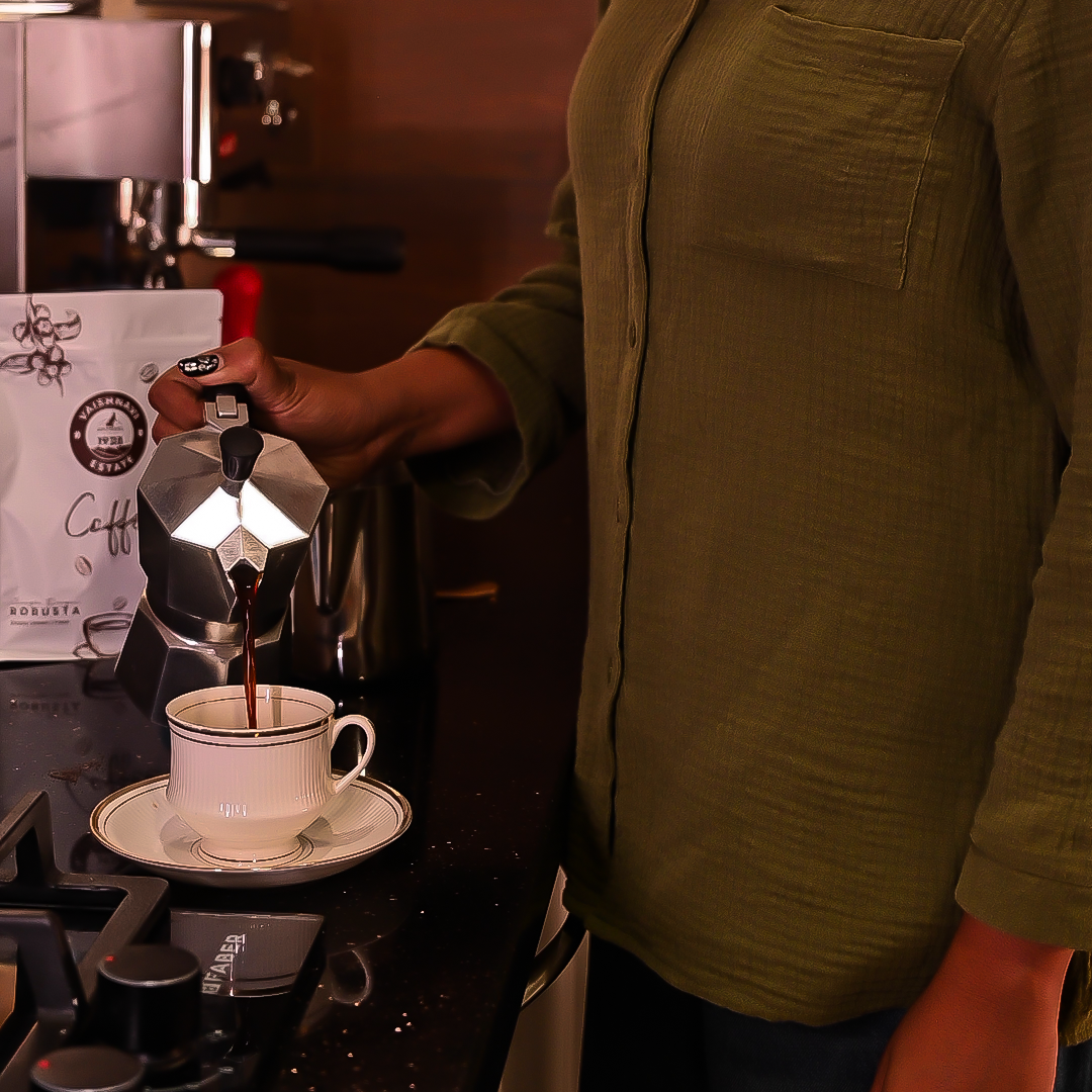 Person pouring Vaishnavi Estate coffee from a Moka pot into a white cup on a stovetop.